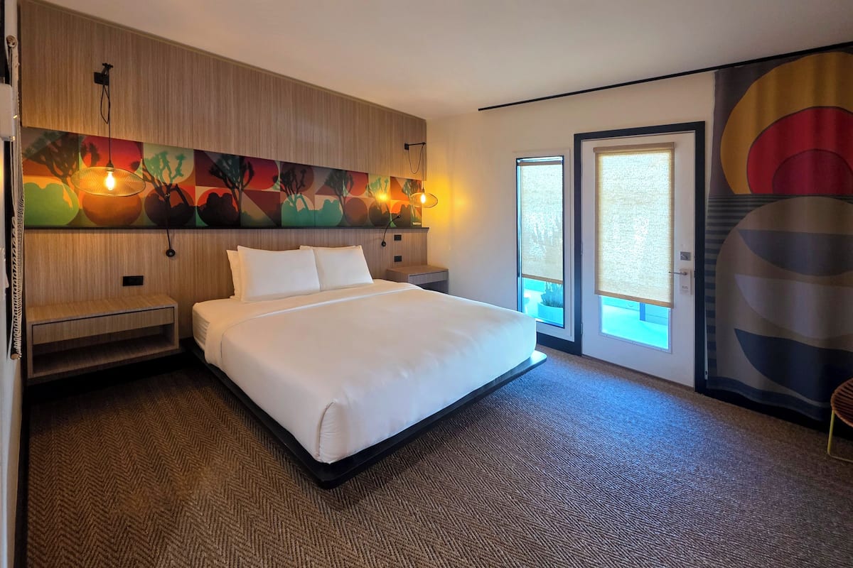 A hotel room with a large bed, a wooden headboard, a wall-mounted artwork, and a door leading to a balcony.