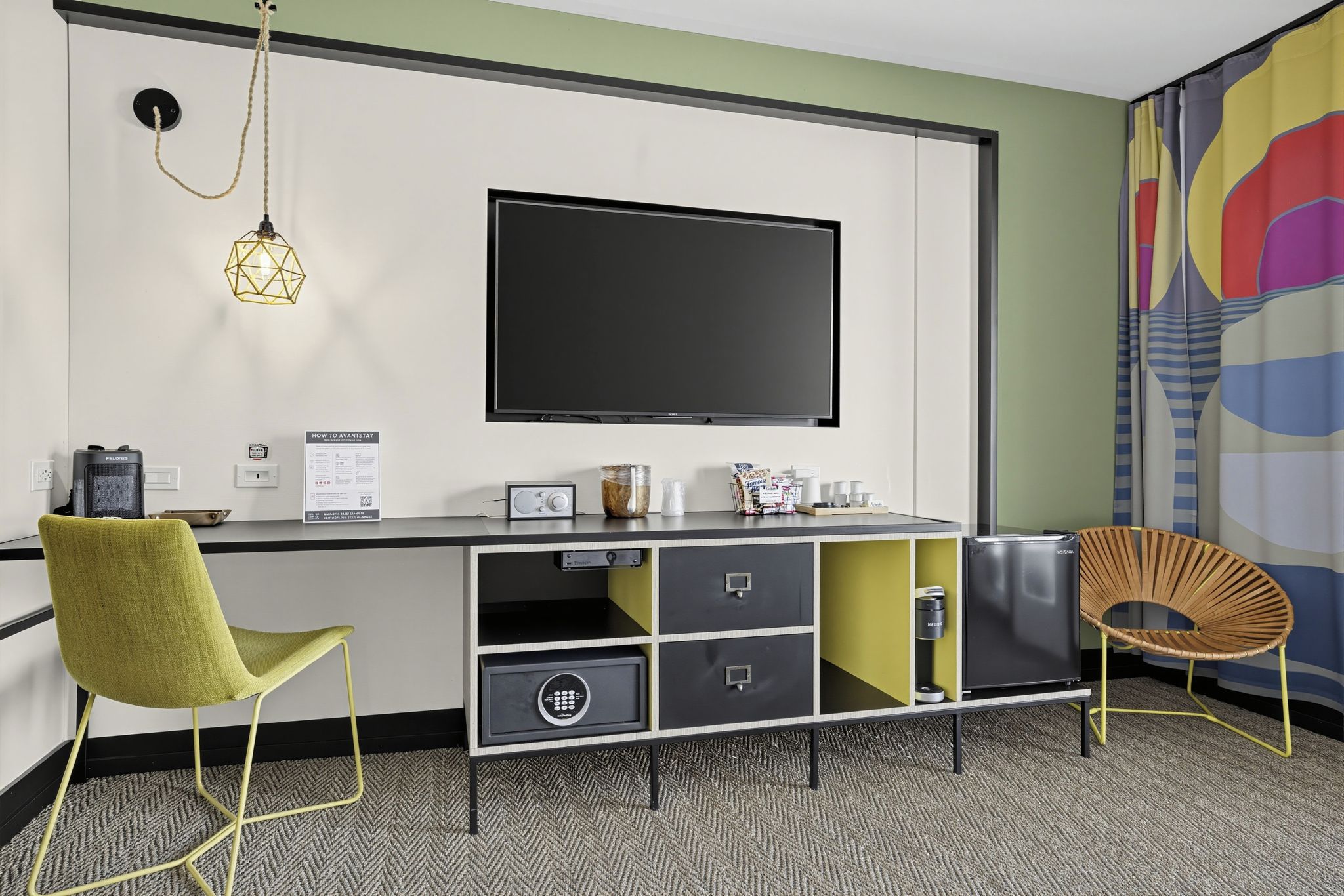 Ein modernes Zimmer mit Flachbildfernseher, Schreibtisch mit Stauraum, Stuhl und einer dekorativen Wandgestalt.