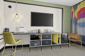 A modern room with a flat-screen TV, a desk with storage, a chair, and a decorative wall piece. - Mahala Hotel by AvantStay (Palm Springs)