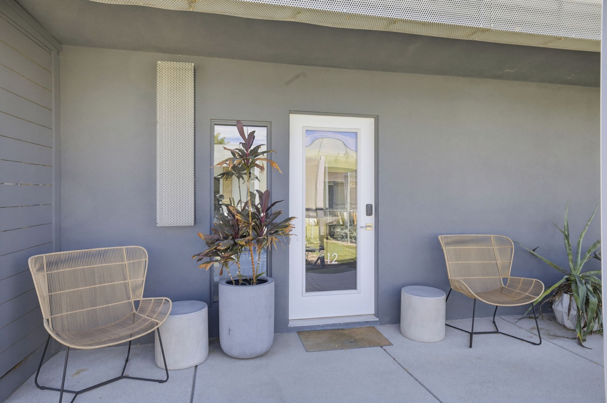 A modern exterior with two wicker chairs, a potted plant, and a door with a number 12.