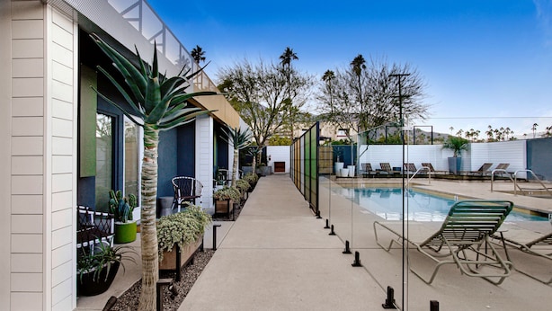 Un espace piscine extérieur moderne, doté de chaises longues, d’un chemin bordé de plantes en pot et offrant une vue dégagée sur la piscine.