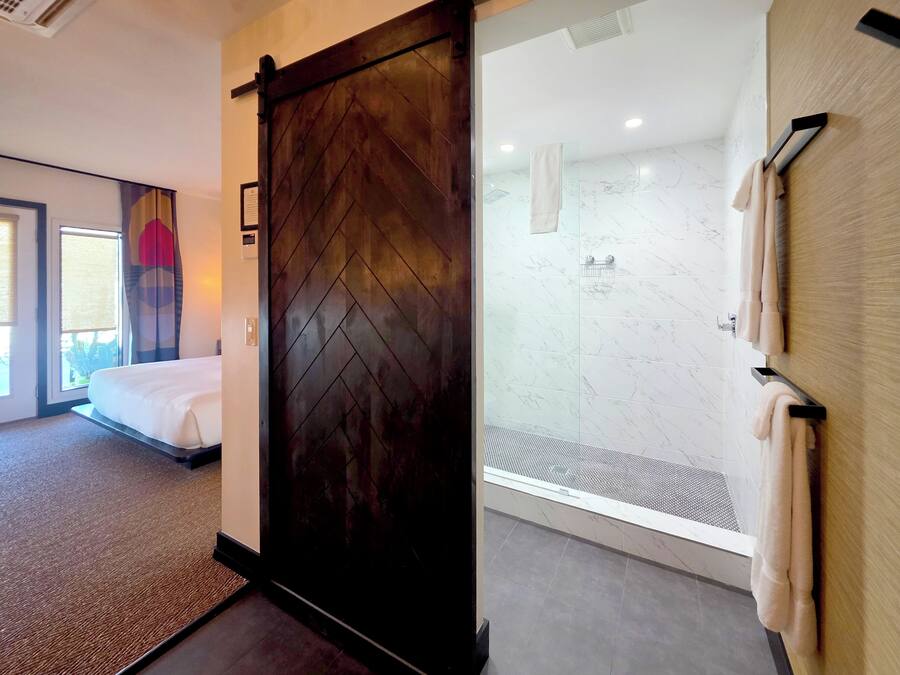 A hotel room with a bed, a sliding door, a shower area with a glass door, and a towel rack.