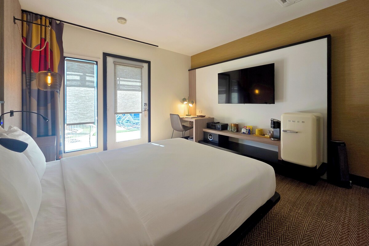 A hotel room with a large bed, a desk with a chair, a television, and a minibar.