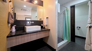 Une salle de bain moderne avec un lavabo rectangulaire, un miroir orné d’un motif hexagonal, un porte-serviettes et un espace douche avec un rideau vert.