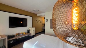 Une chambre d’hôtel équipée d’un lit, d’un téléviseur fixé au mur, d’un petit réfrigérateur et d’un luminaire décoratif.