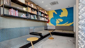 Un espace de détente moderne avec des sièges à motifs, une bibliothèque et une grande fresque murale abstraite.