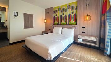 Una habitación de hotel moderna con una cama grande, un cabecero con un mural colorido, una mesita de noche con una lámpara y un estante pequeño.