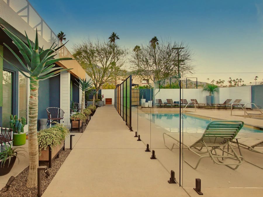 A poolside area with lounge chairs, a pool, and a pathway lined with plants and a chair.