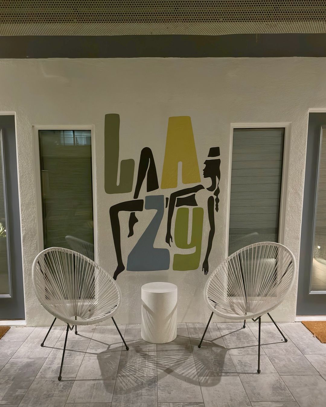 A room with two white wireframe chairs, a small white table, and a wall with large, colorful letters.