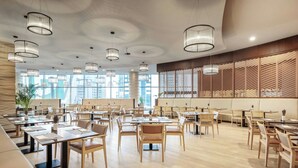 A spacious restaurant with multiple tables and chairs, large windows, and modern pendant lighting. - Le Méridien City Center, Doha (Doha)
