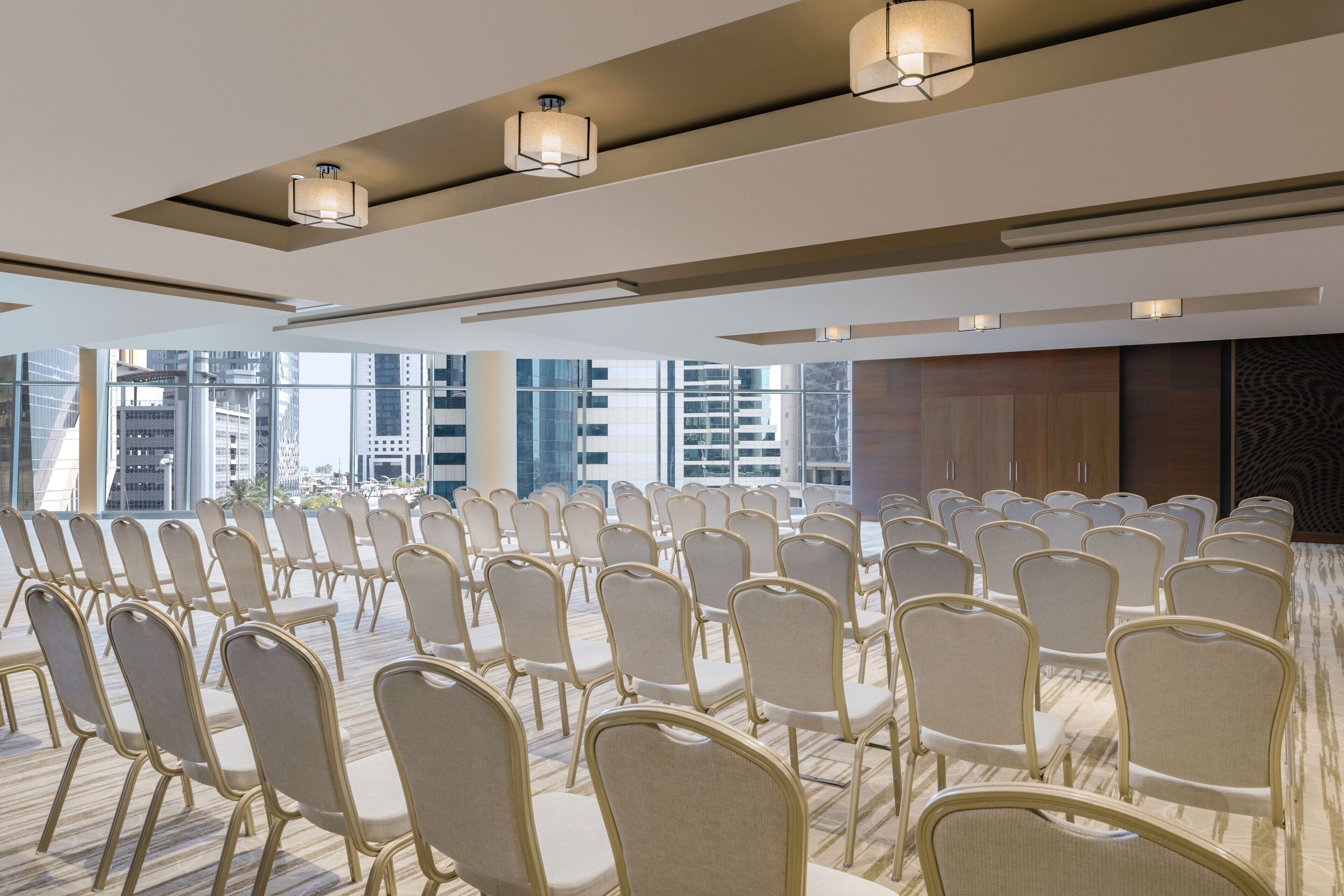 Een congreszaal met rijen stoelen, grote ramen en moderne verlichtingsarmaturen.