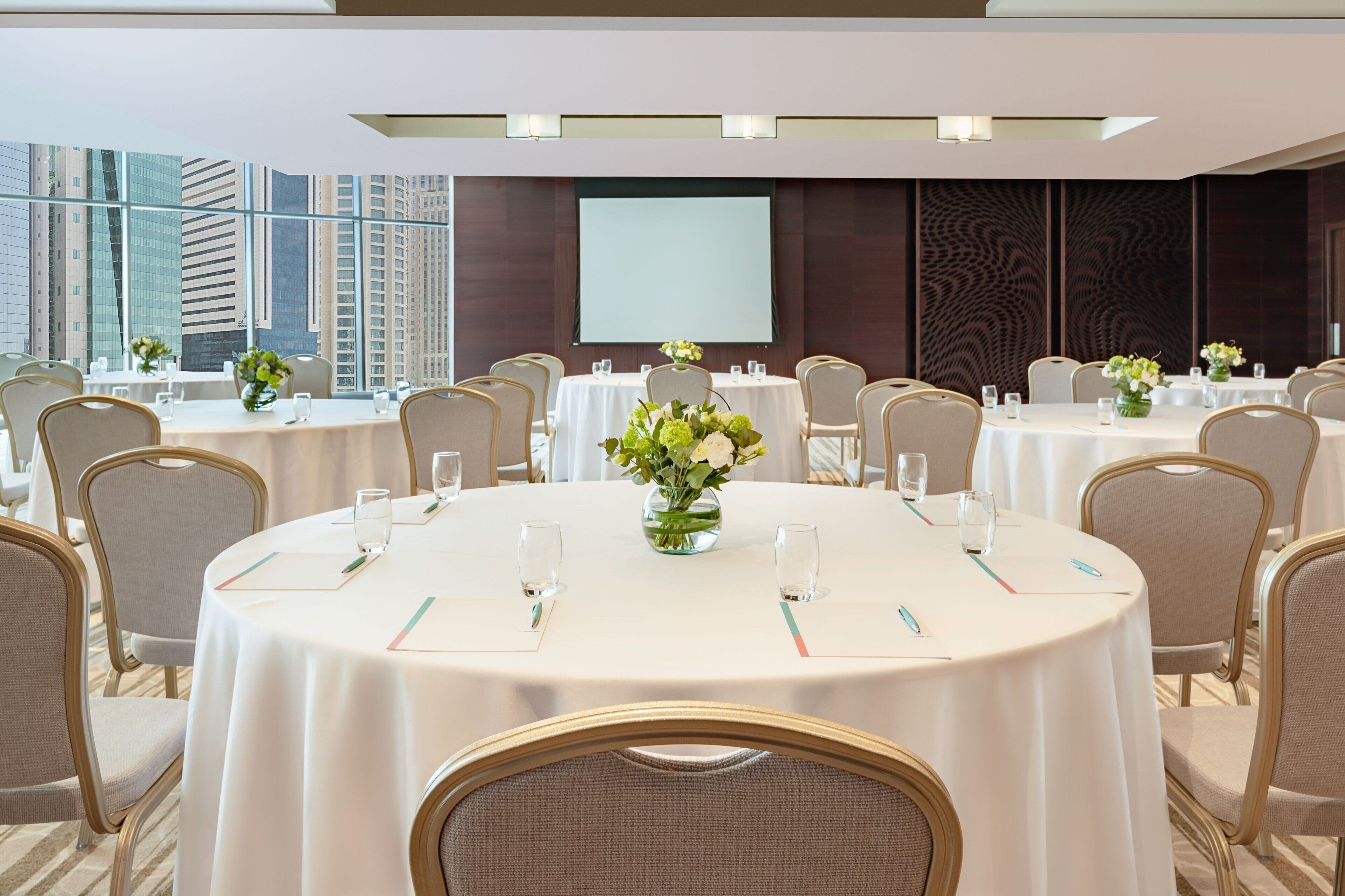 A conference room with multiple round tables, each with a white tablecloth, chairs, and floral centerpieces.