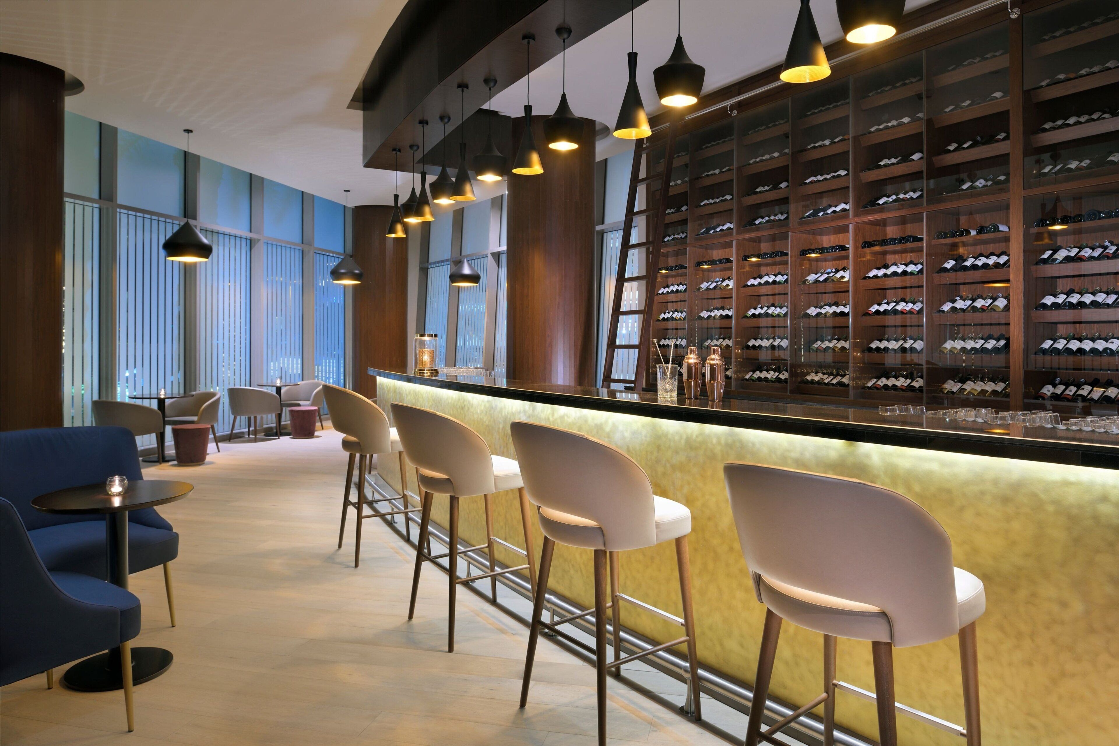 Een bar met hoge stoelen, een wijnrek en hanglampen.