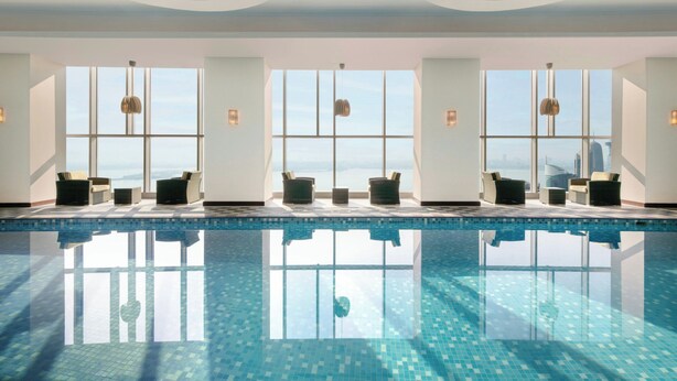 A modern indoor swimming pool with clear glass walls, allowing views of the cityscape. - Le Méridien City Center, Doha (Doha)