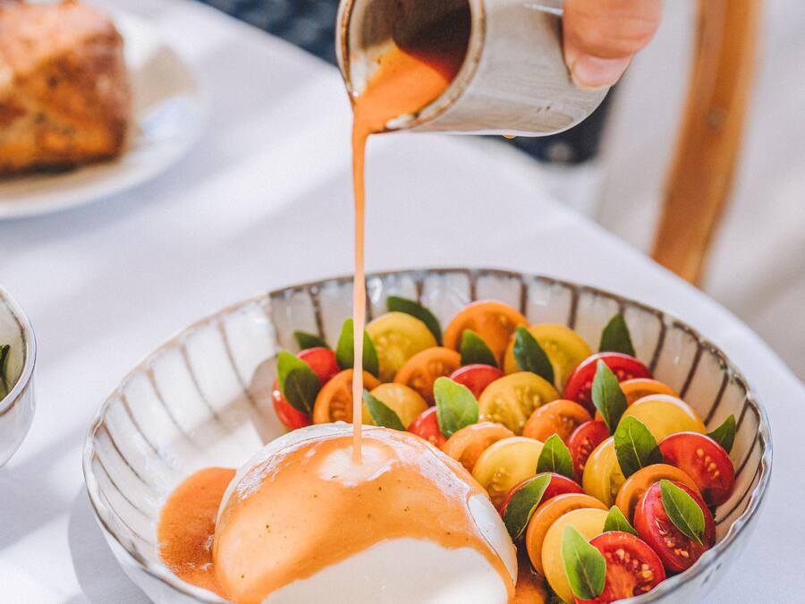 En skål med skivad frukt och ett pocherat ägg med sås som hälls över.