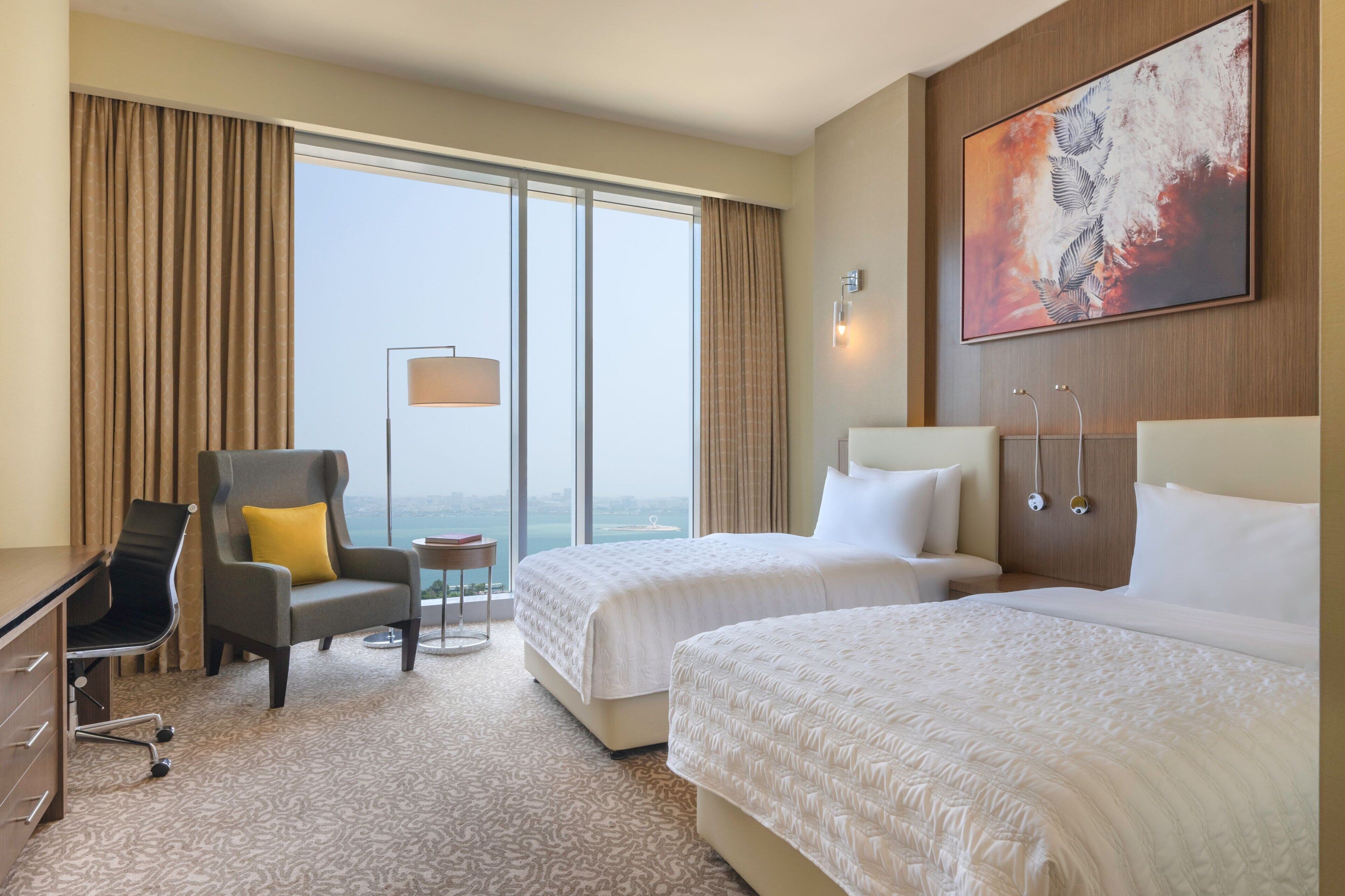 A hotel room with two beds, a desk, a chair, a small table, and a large window with curtains.