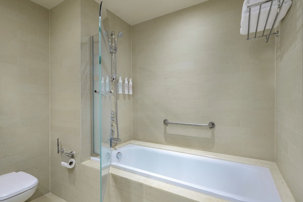Un baño con ducha envuelta en vidrio, una bañera, un inodoro y un perchero para toallas.