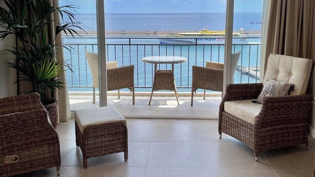 A balcony with wicker furniture, a view of the sea, and a large window.