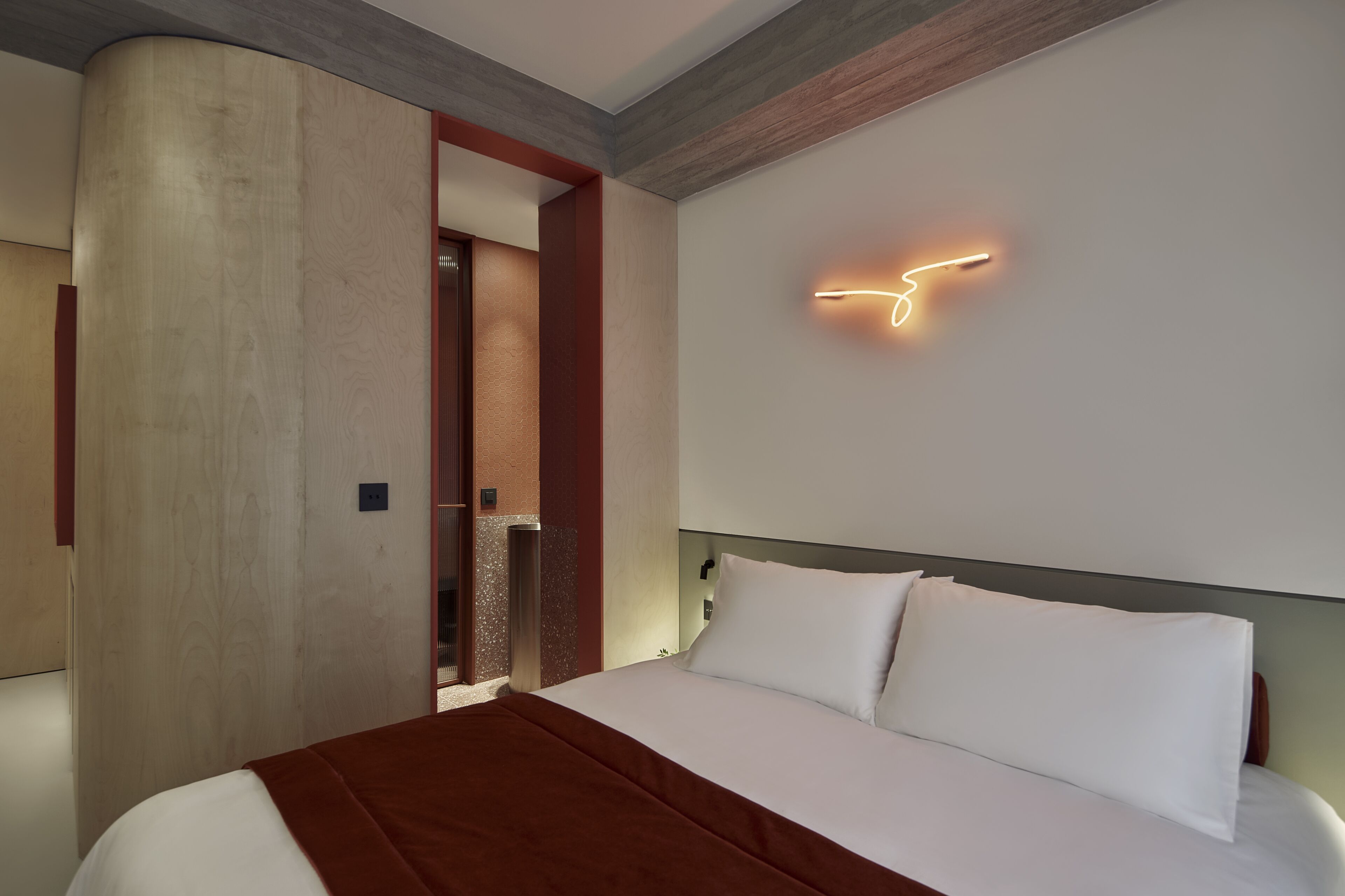 A modern hotel room with a large bed, a wooden headboard, and a wall-mounted light fixture.