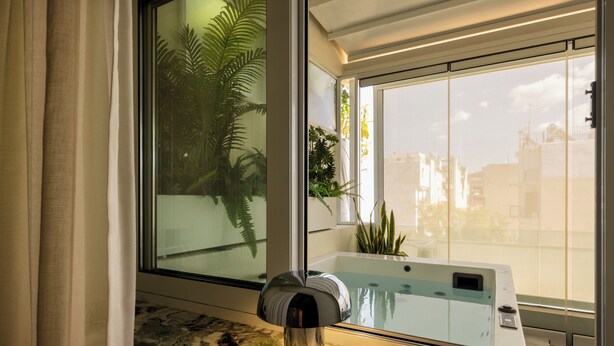 A bathroom with a glass-enclosed bathtub, a marble countertop, and a window with curtains. - The Newel Metaxourgeio by Athens Stay (Athens)