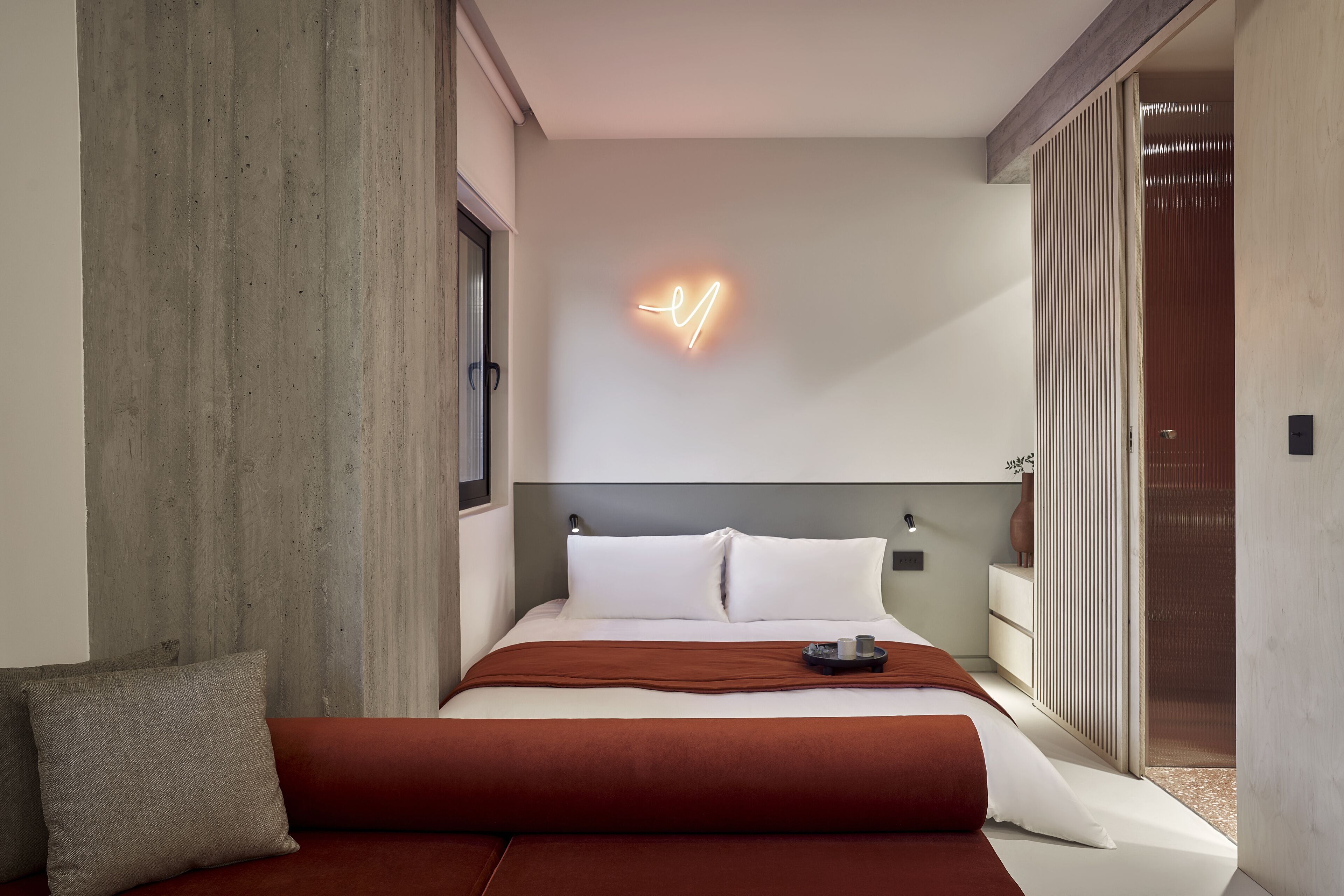 Una habitación de hotel moderna con una cama grande, un letrero de neón y una puerta corredera.