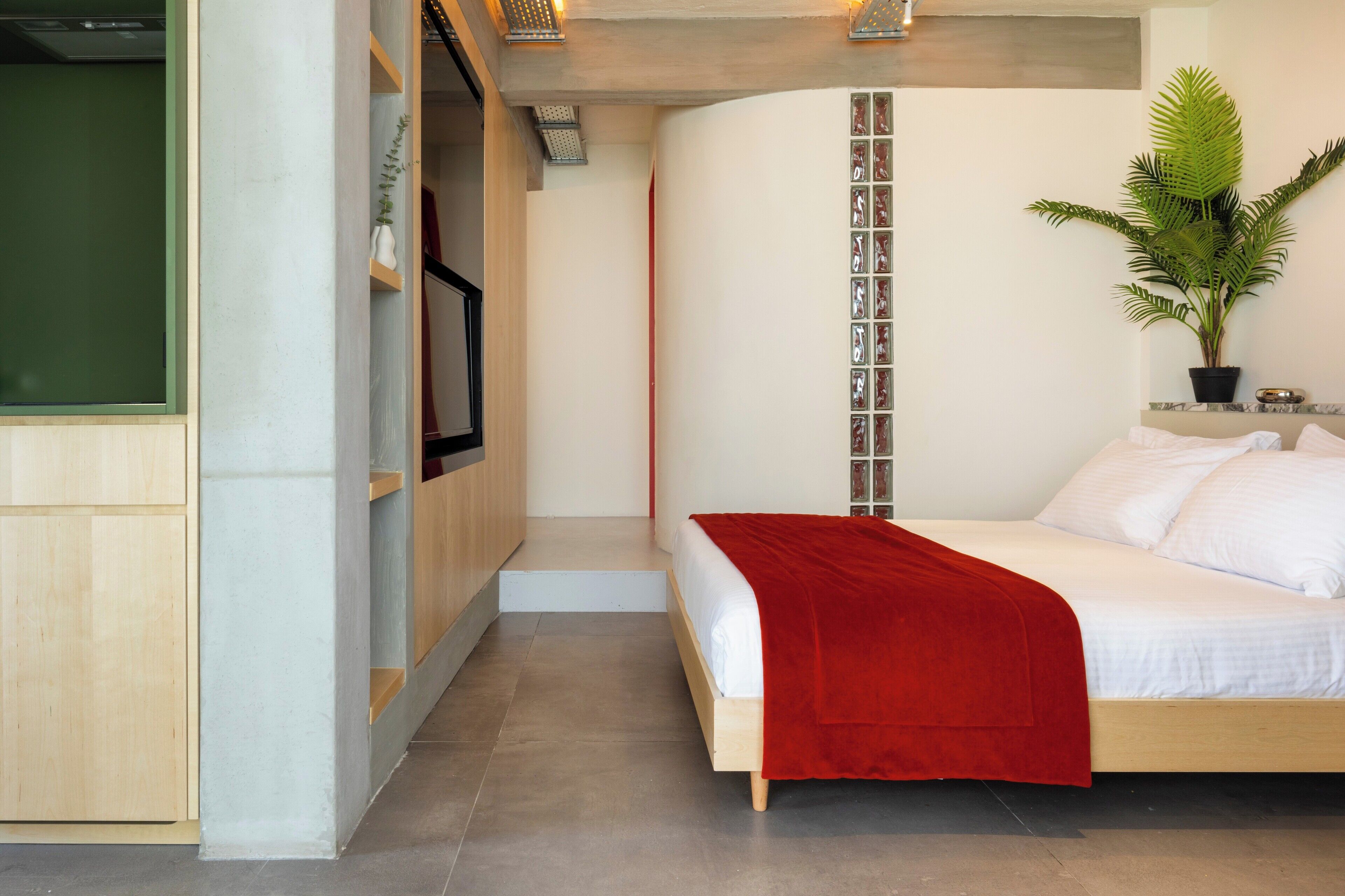 Une chambre à coucher moderne avec un lit, un plaid rouge, une plante en pot et une armoire en bois.