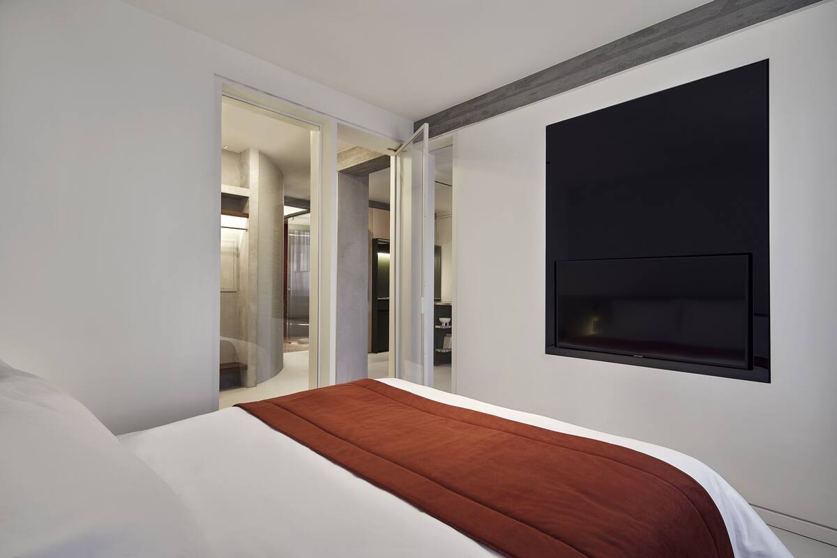 A modern hotel room with a large bed, a flat-screen TV mounted on the wall, and a walk-in closet.