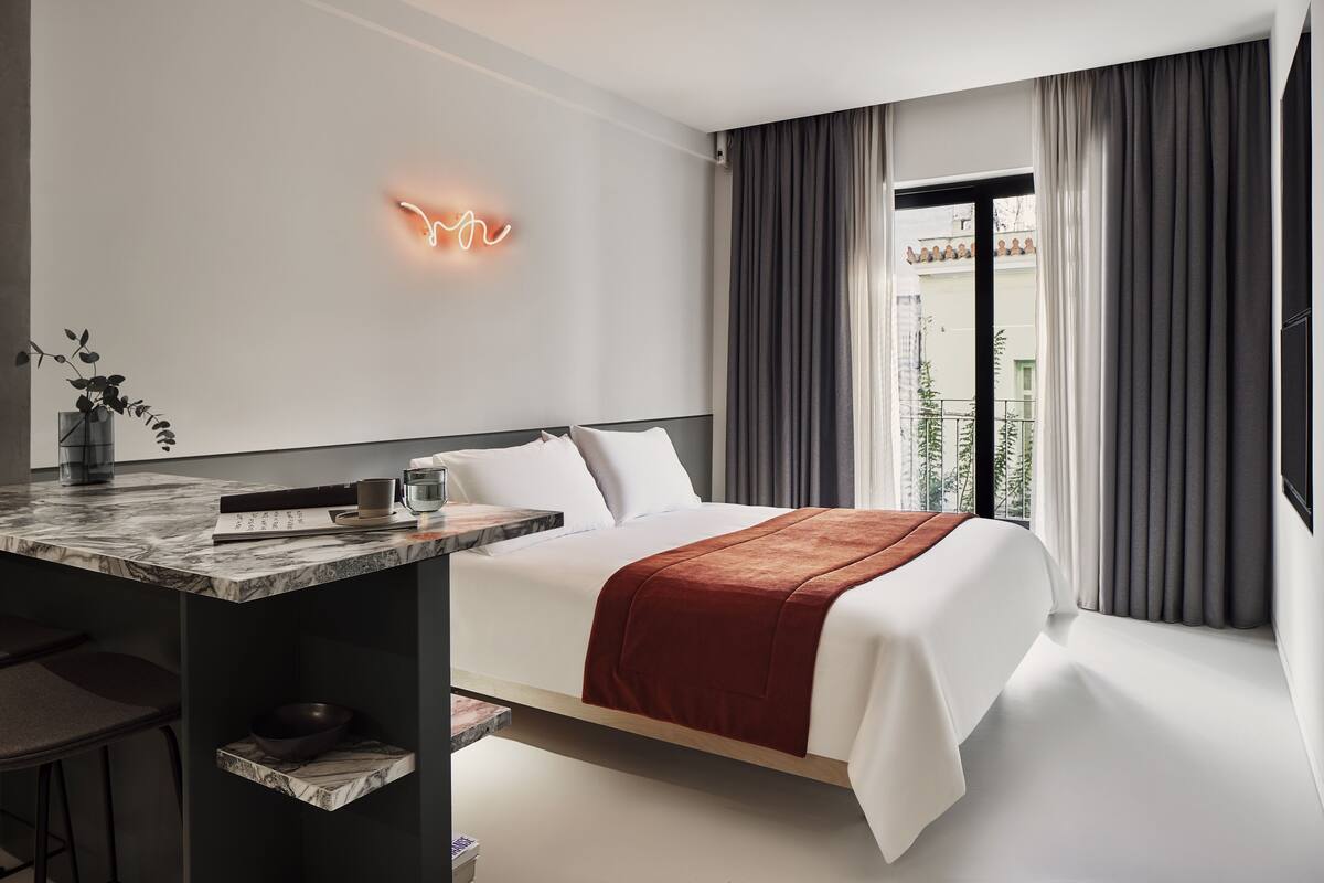 A modern hotel room with a bed, bedside table, and a neon sign on the wall.