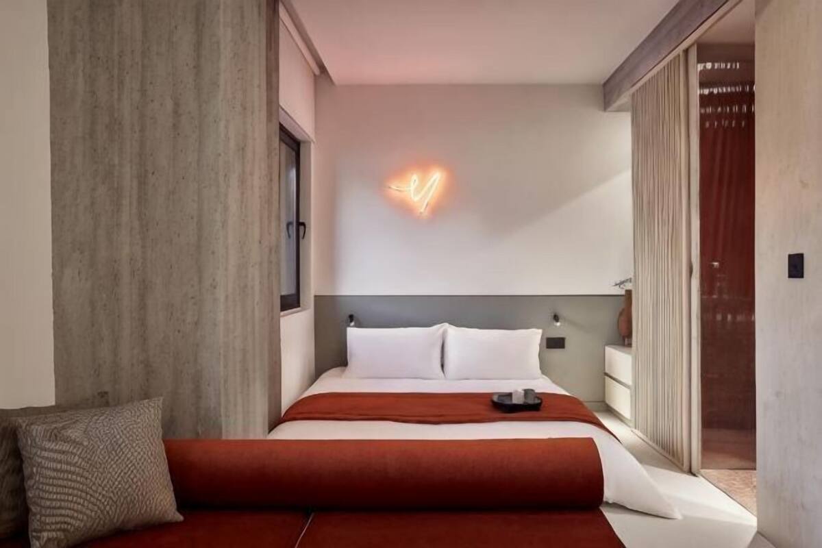 A modern hotel room with a bed, bedside table, and a neon light on the wall.