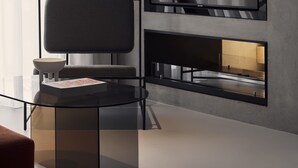 A modern living room with a large flat-screen TV mounted on a wall, a glass coffee table, a minimalist chair, and a view of the outdoors through sheer curtains. - The Newel Metaxourgeio by Athens Stay (Athens)