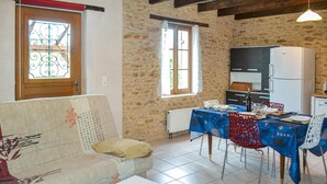 Ein gemütliches Wohnzimmer mit einer Couch, einem Esstisch für zwei Personen und einer Küchenzeile inklusive Kühlschrank und Schränken.