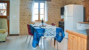 Ein Essbereich mit Tisch für zwei Personen, einem fensterbelaubten Fenster, einem Kühlschrank und einer Küchenarbeitsplatte.