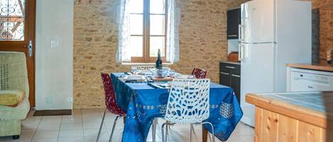 Un comedor con una mesa dispuesta para dos, una ventana con cortinas, un refrigerador y una encimera de cocina.