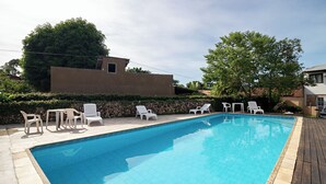 Piscina retangular com borda em azulejo, rodeada por espreguiçadeiras brancas e uma parede de pedra.