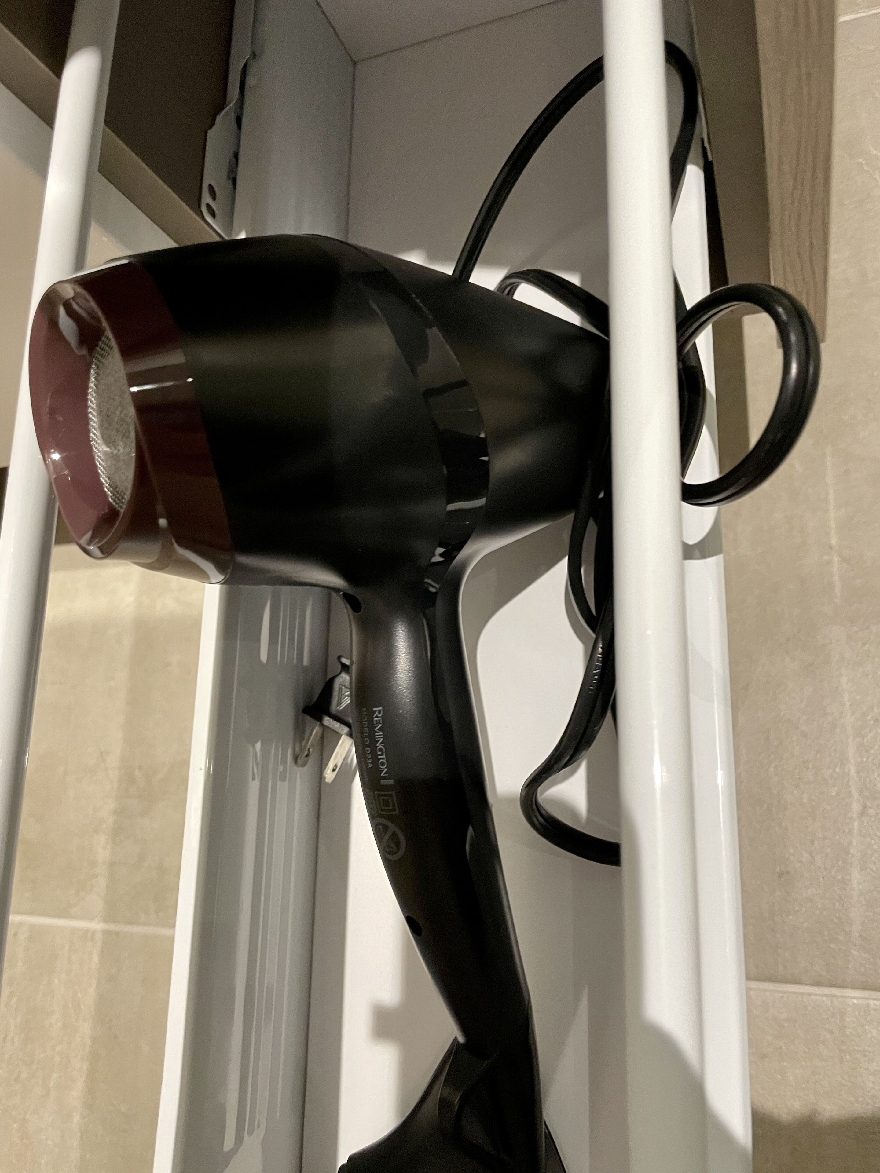 Un sèche-cheveux dont le cordon est branché à une prise électrique blanche.