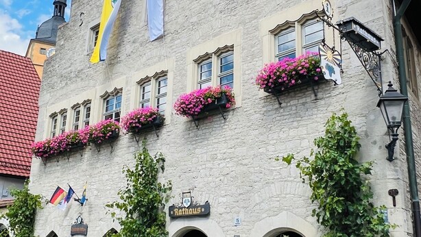 Un edificio histórico de piedra con numerosas ventanas, algunas con jardineras, y un letrero que dice 