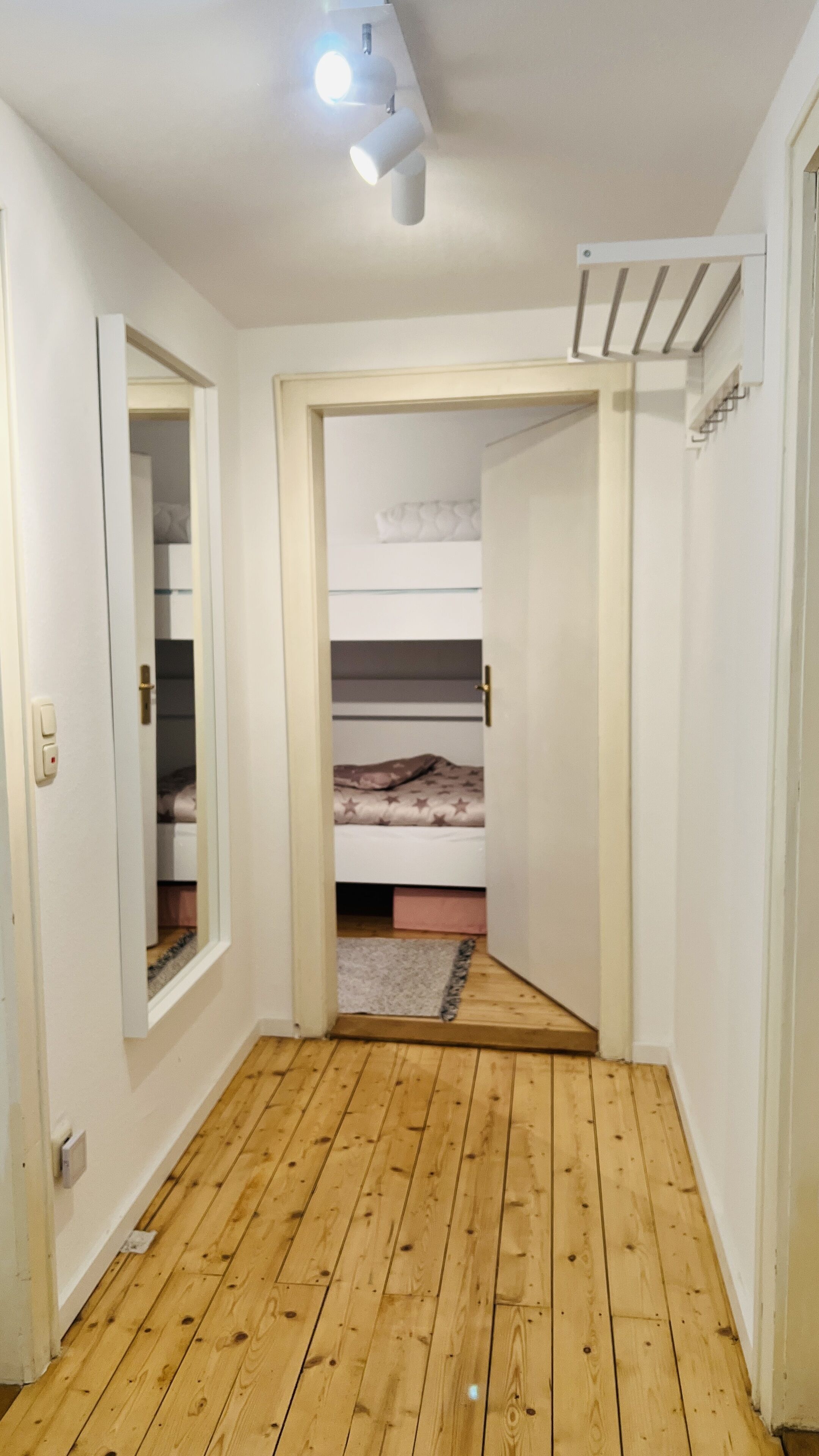 Ein schmaler Flur mit Holzdielen, der zu einem Schlafzimmer mit Etagenbett führt.