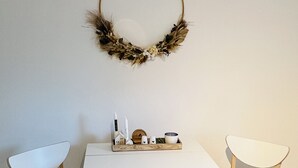 Un comedor con una mesa blanca y dos sillas blancas, suelo de madera y un adorno en la pared.
