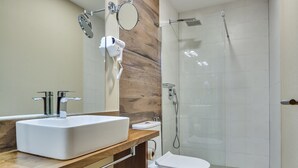 Een moderne badkamer met een grote witte wastafel, een houten wastafelmeubel, een toilet en een douchecel met glazen wanden.