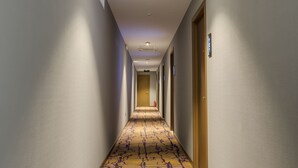 Een hotelgang met een vluchtwegbord, bekleed met tapijt, en deuren aan beide kanten.