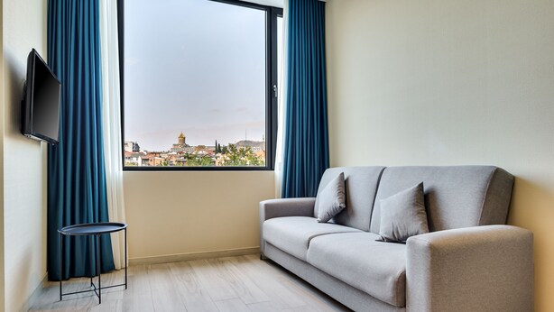 Een moderne woonkamer met een bank, een bijzettafeltje en een aan de muur bevestigde televisie.