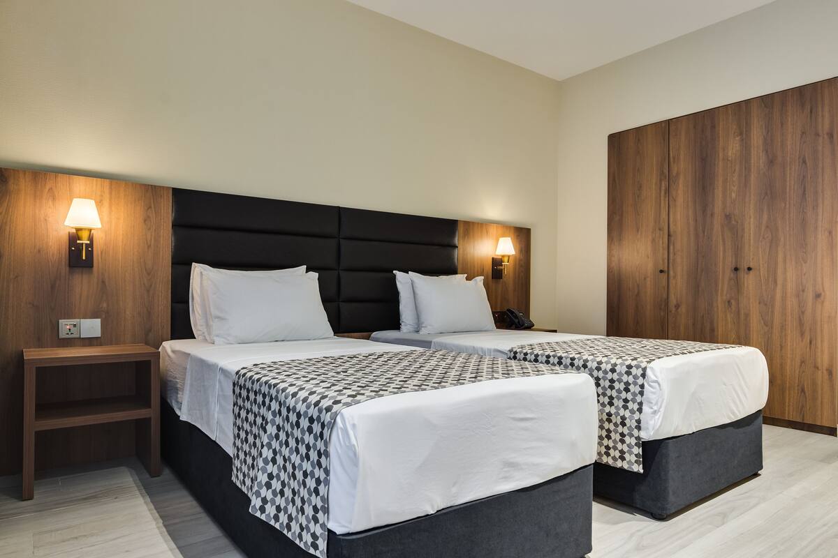 A hotel room with two beds, a wooden wardrobe, and bedside lamps.
