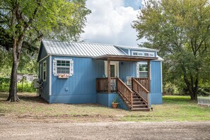 A small, single-story house with a blue exterior, a wooden front porch, and a staircase leading to the entrance. - Amazing Log Home on 4 acres (Granbury)