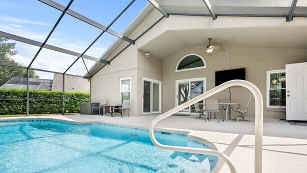 A swimming pool with a glass ceiling, outdoor furniture, and a door leading to a covered patio area.