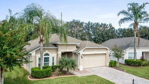 A single-story house with a garage, surrounded by well-maintained lawns and palm trees.