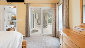 A bedroom with a bed, a dresser, a television, and a sliding glass door leading to a patio area with outdoor furniture.