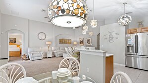 A modern kitchen with a central island, stainless steel appliances, and a dining area with white chairs and a glass table.