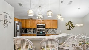 A kitchen with wooden cabinets, a built-in microwave, and a refrigerator. There are wicker chairs around a central island.