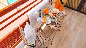 A balcony with a pool view, a table with breakfast items, and a chair with a towel. - Delight Holiday Home (Playa del Inglés)