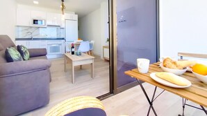 A modern living room with a sofa, a dining table with breakfast items, and a kitchen in the background. - Delight Holiday Home (Playa del Inglés)
